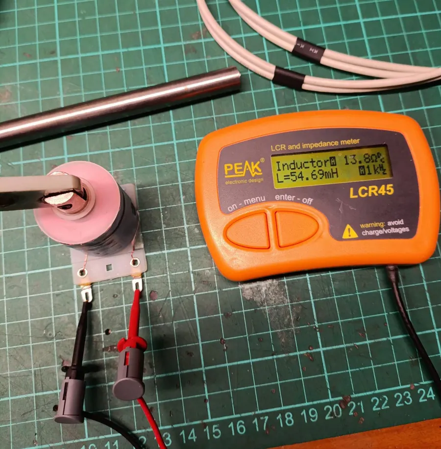 A Peak LCR45 LCR meter reading 54.69 millihenries and 13.8 ohms at 1 kHz on an AE-26-1500 coil with a flipper armature and link inserted in its bore.