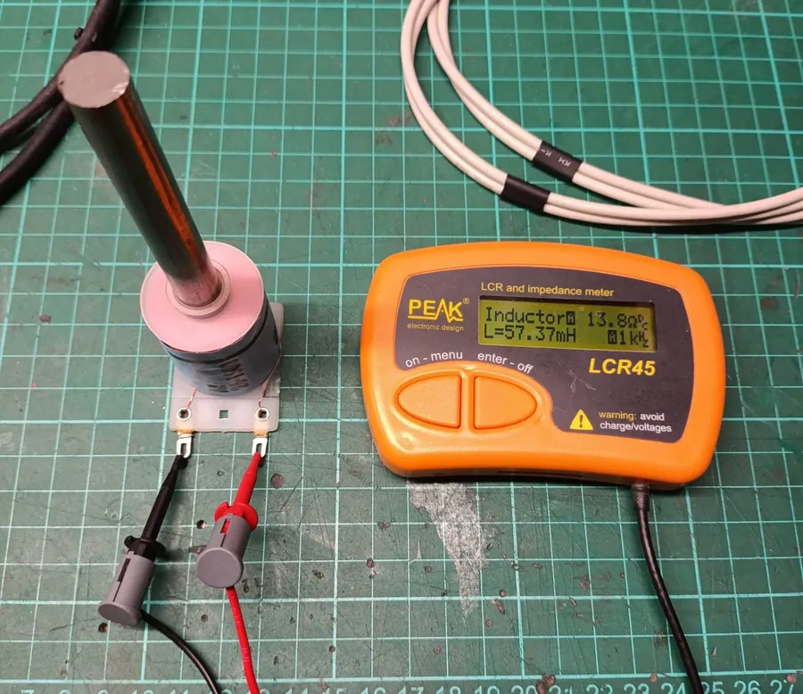 The same Peak LCR45 LCR meter reading 57.37 millihenries at 1 kHz on the same coil with a 10 cm bright steel rod standing in its bore.
