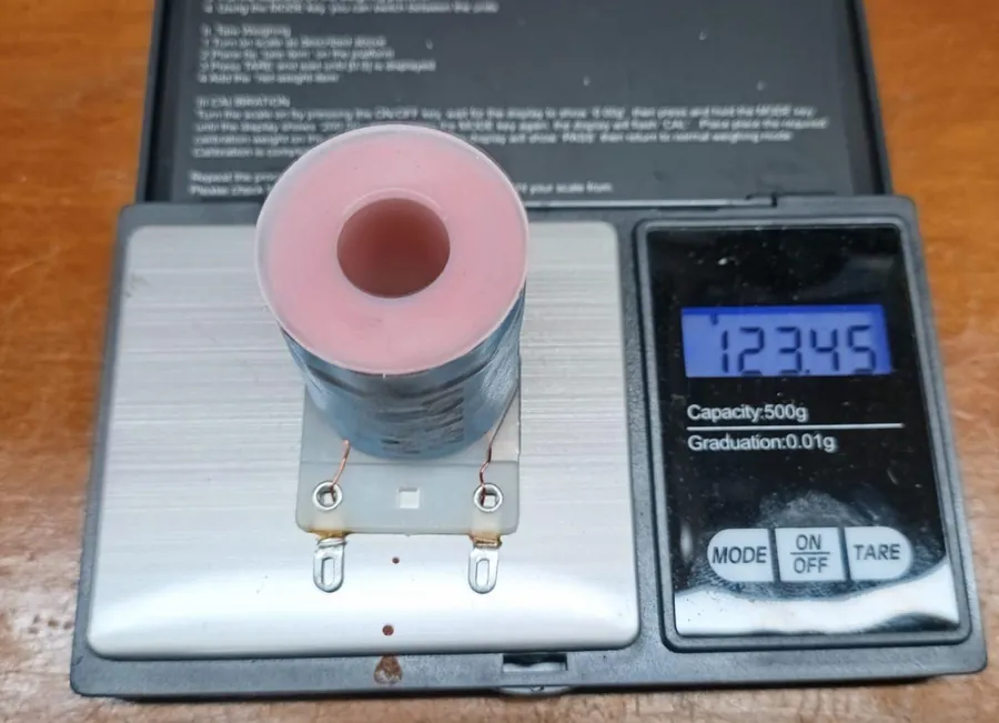 An AE-26-1500 coil standing on a pocket digital scale reading 123.45 grams, with 500 g capacity and 0.01 g graduation printed on the scale.