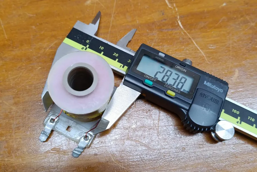 A Mitutoyo digital caliper reading 28.38 millimetres across the outside of the paper-wrapped winding of a yellow-labelled coil.