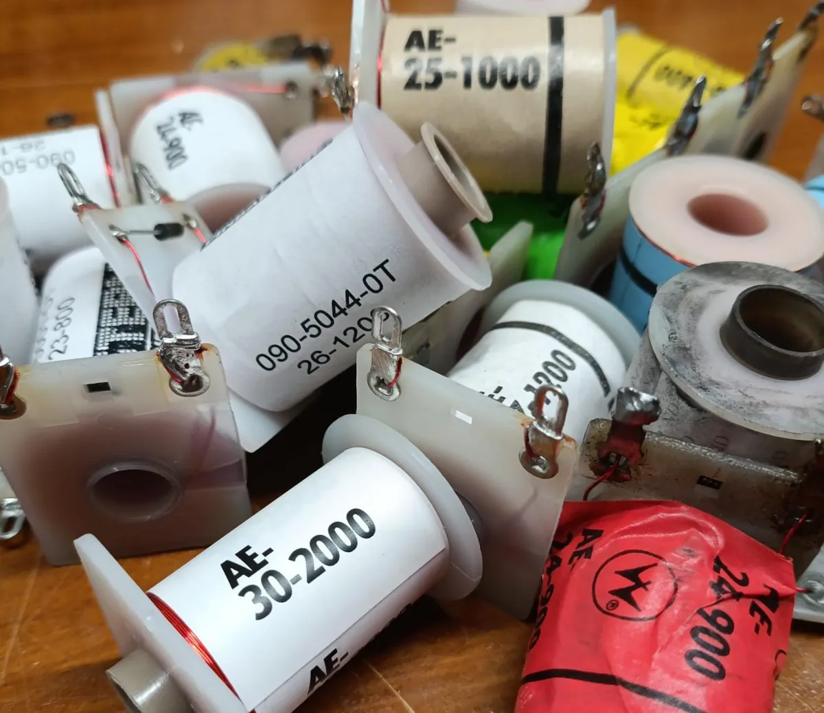 A heap of pinball coils with printed labels including AE-25-1000, AE-30-2000, AE-24-900 and 090-5044-OT 26-1200
