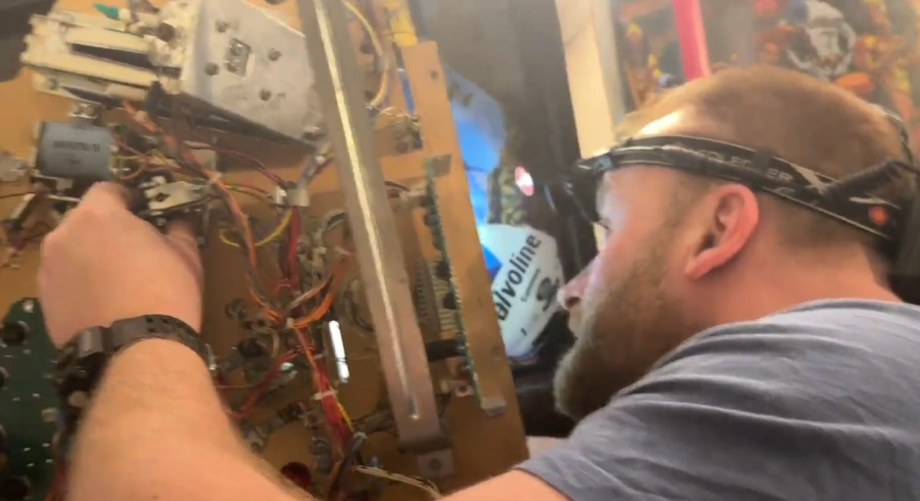 Man with a head torch working on the underside of a pinball playfield