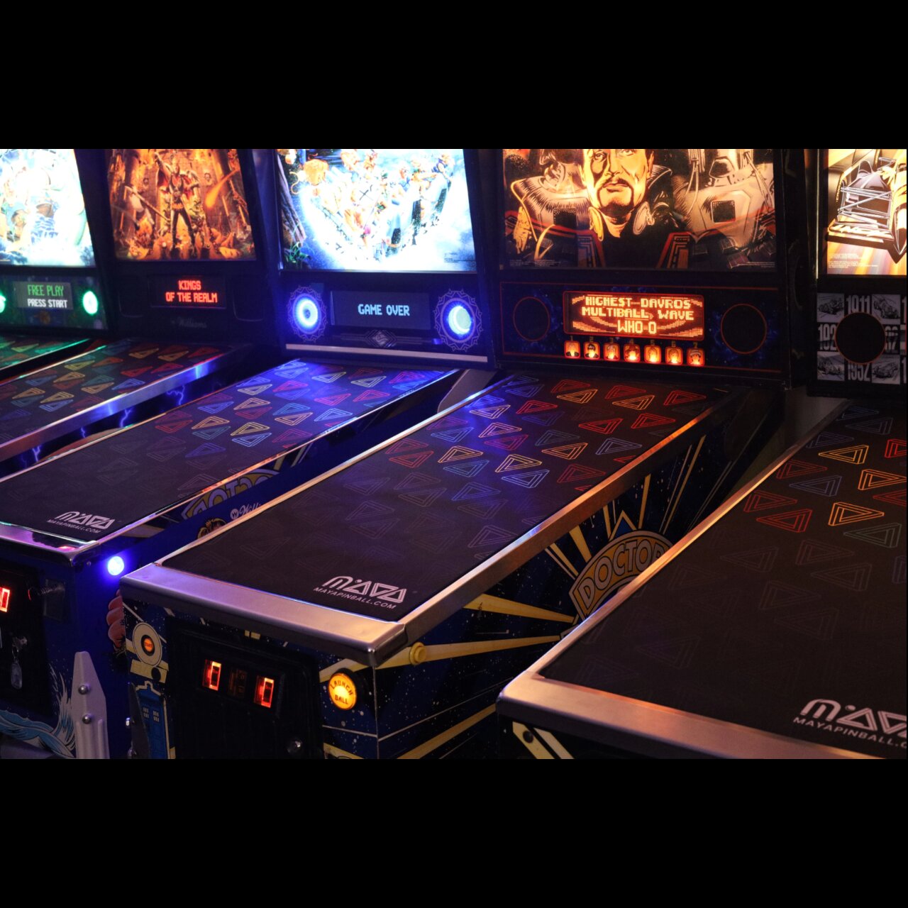 MAYA Glass Defenders fitted across a row of lit pinball machines in a dark arcade